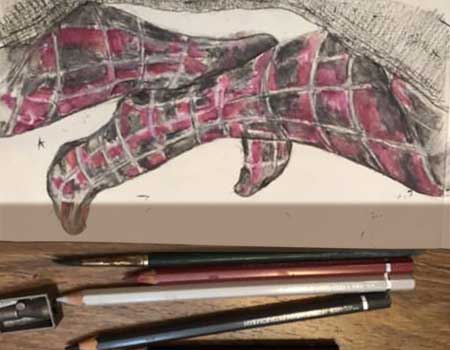 Colored pencil sketch of woman's purple and black checked tights, sitting cross-legged on sofa with colored pencils and sharpener in front of drawing.