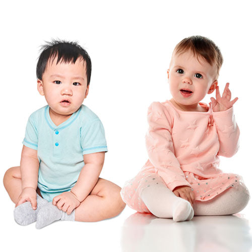 To adorable babies sitting against a white background, left side is Asian boy in blue t-shirt and grey socks, right side is white girl in pink top and skirt and white tights, hand to ear.