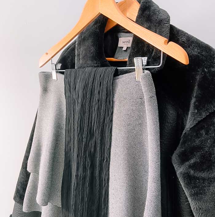 Garments stylishly hanging on wooden hangers: black fleece dress jacket and black patterned tights draped over short layered pale grey skirt.
