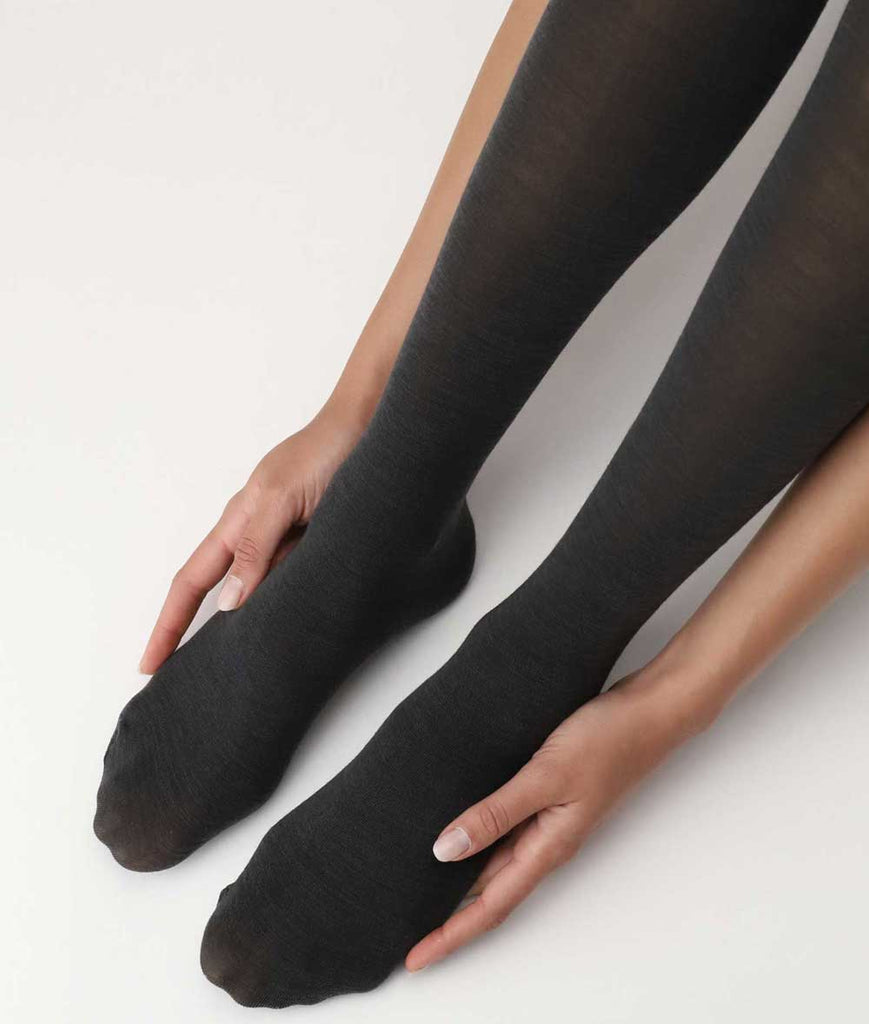 Angled close up of woman's legs from calves to toes in opaque black tights, hands resting gently either side of feet.