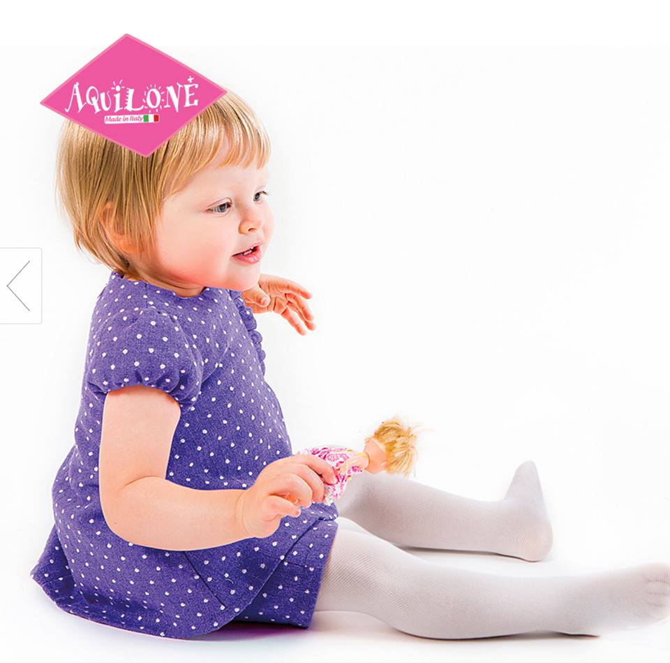 Toddler sitting, wearing a blue dress and white sheer tights.