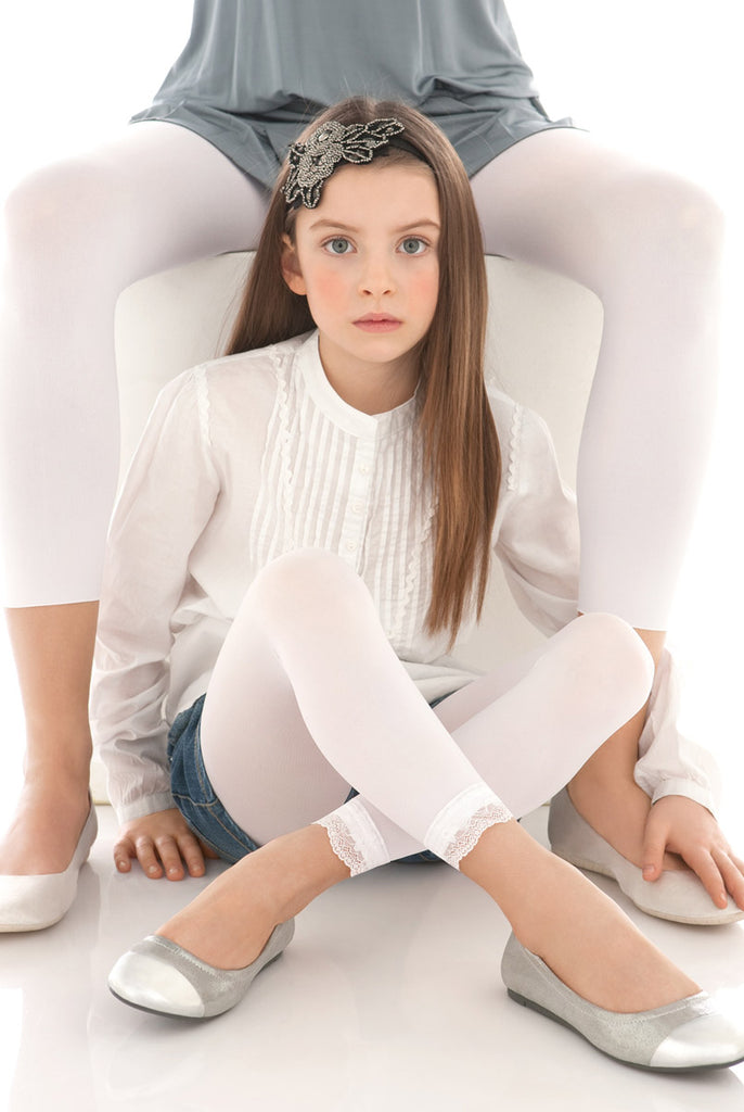 Young girl sitting with legs crossed in white lace footless tights and ballerina flats.