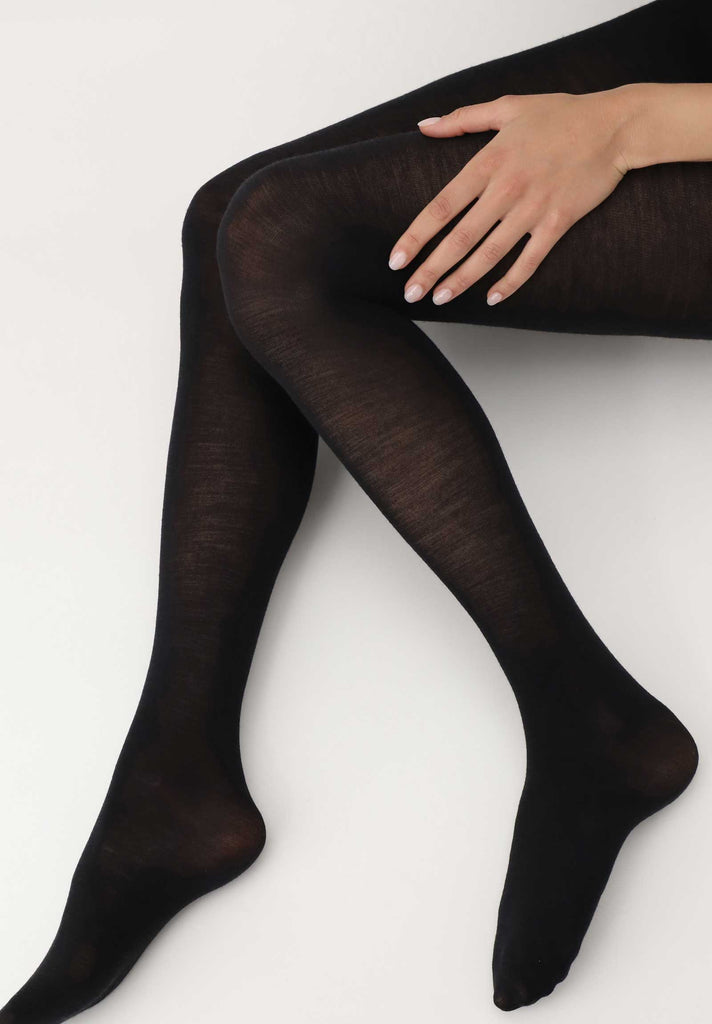 Lady's legs in sitting position, wearing black tights, bent at the knees, with one hand on the side of her left leg,