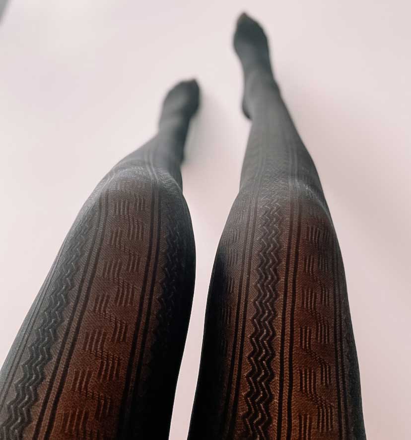 Women's legs in black ribbed opaque tights, photographed from mid-thigh down to toes, transitioning into soft focus at toes.