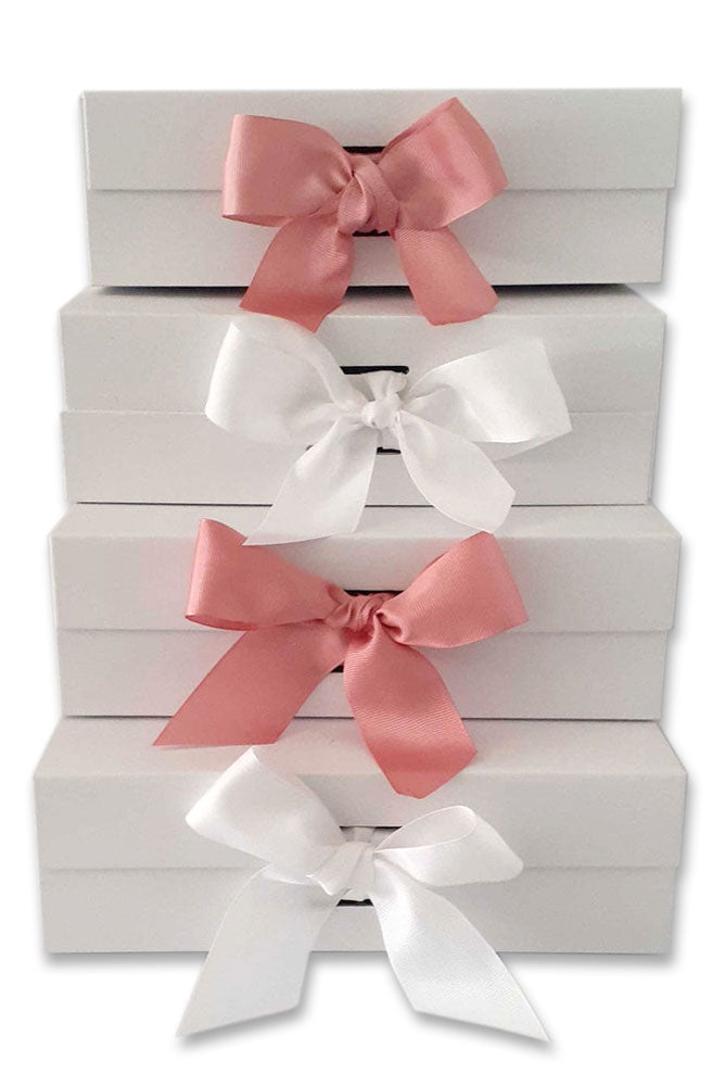 Stack of four large, flat white gift boxes, tied in front with alternating pink and white bows.