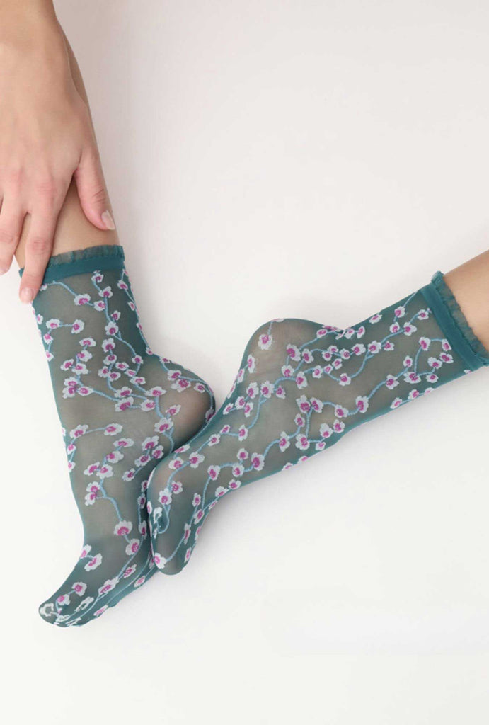 Lady's feet touching via the soles, wearing green, floral pattern socks.