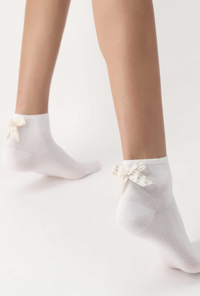 Lady's feet, wearing white, ankle socks with with and ecru striped bows.