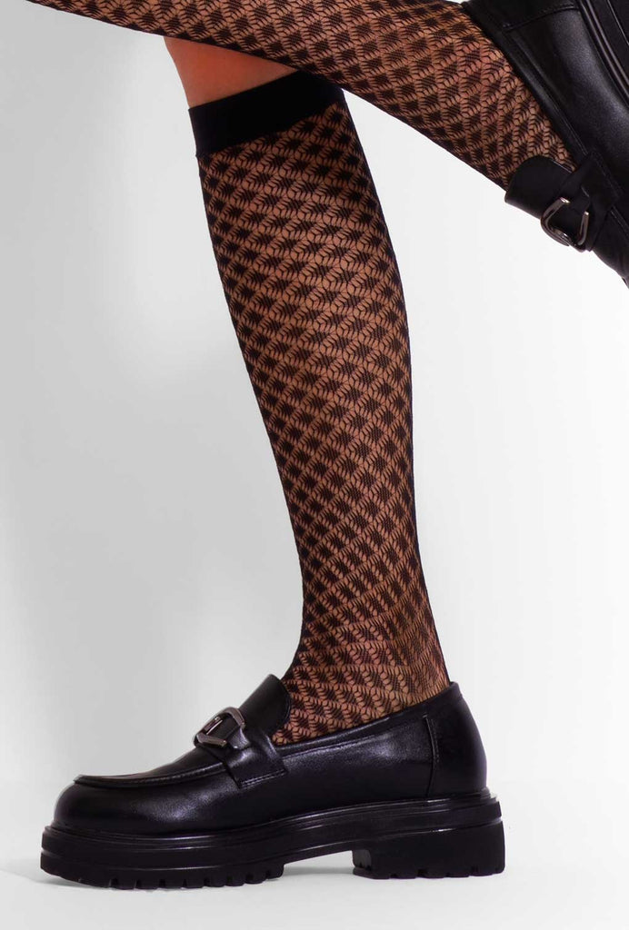 Side view of lady's calf wearing black patterned fishnet knee highs.