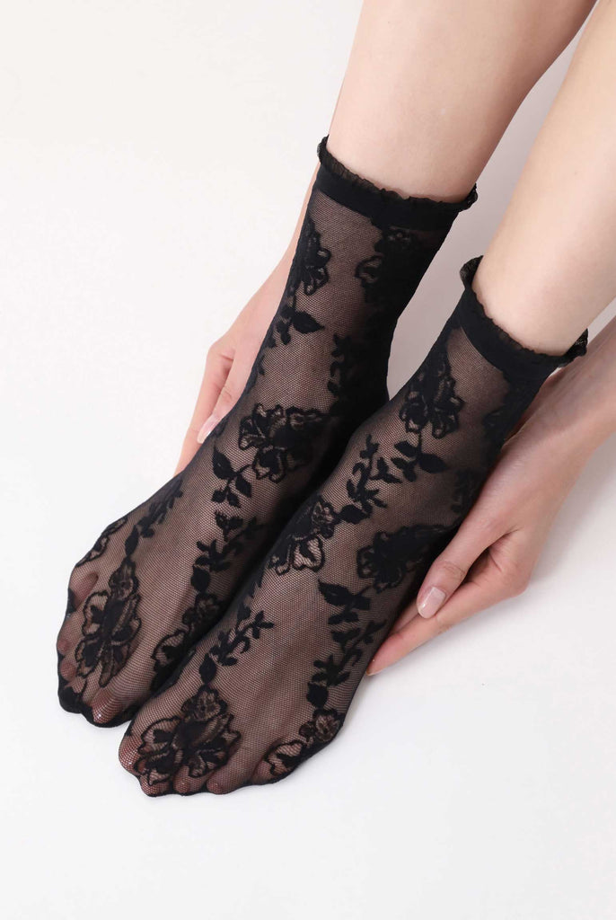 Front view of lady's feet held within a lady's hands and wearing black lace crew socks.