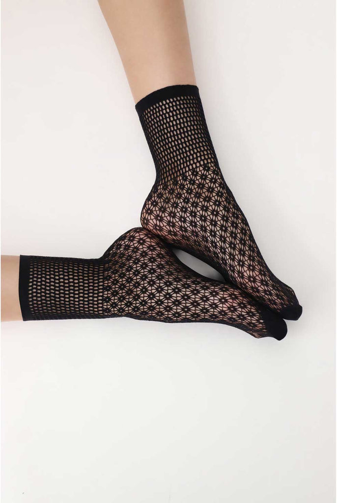 The soles of a woman's feet touching, wearing black patterned mesh socks.
