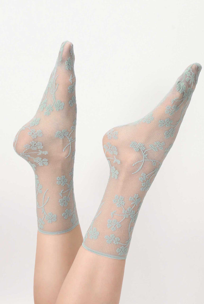 Ladies feet, in the air, showcasing idro-green, floral pattern sheer socks.
