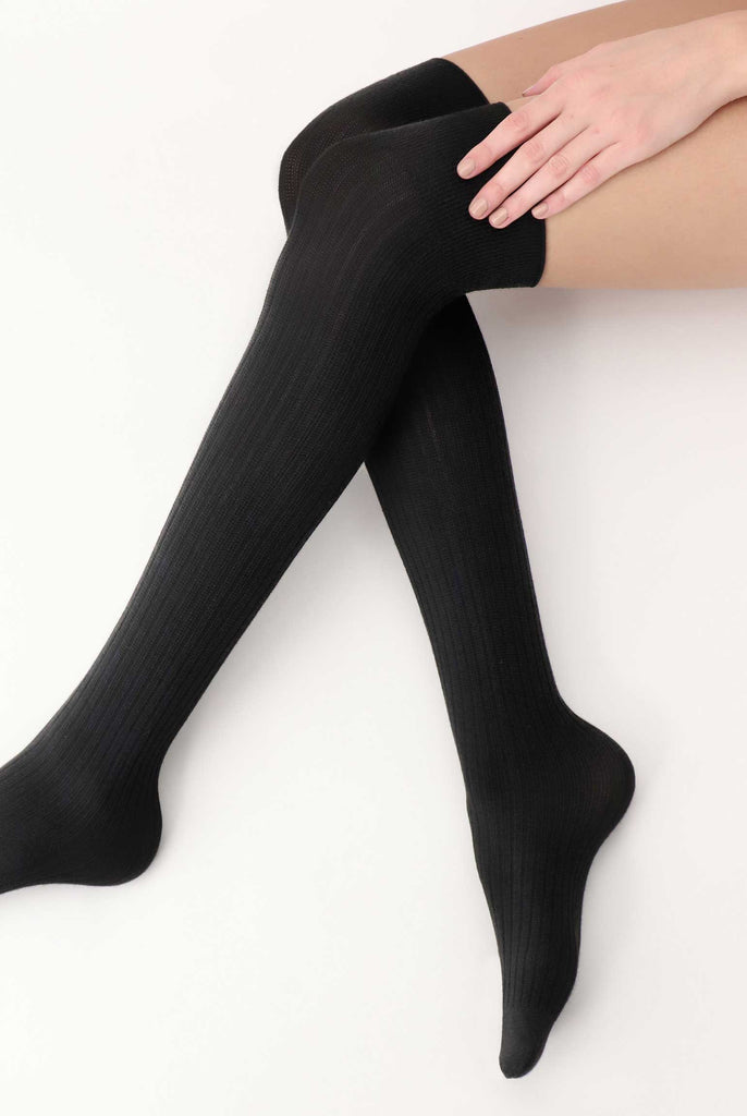 Ladies legs, criss crossed, wearing black over the knee socks.