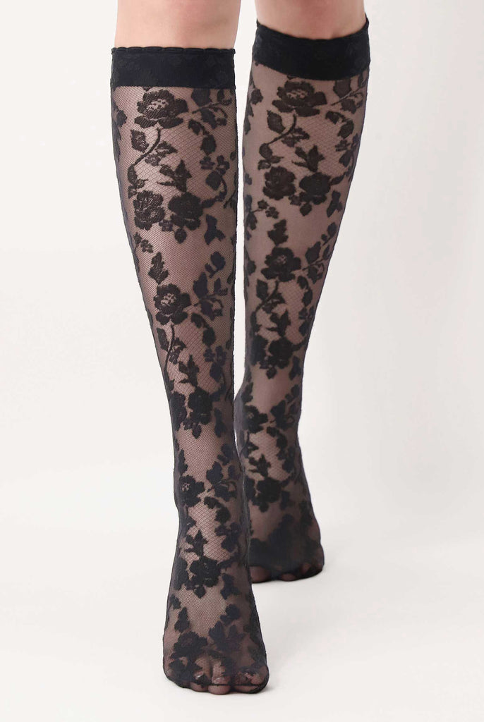 Front view of lady's calves and feet in black floral lace knee highs.