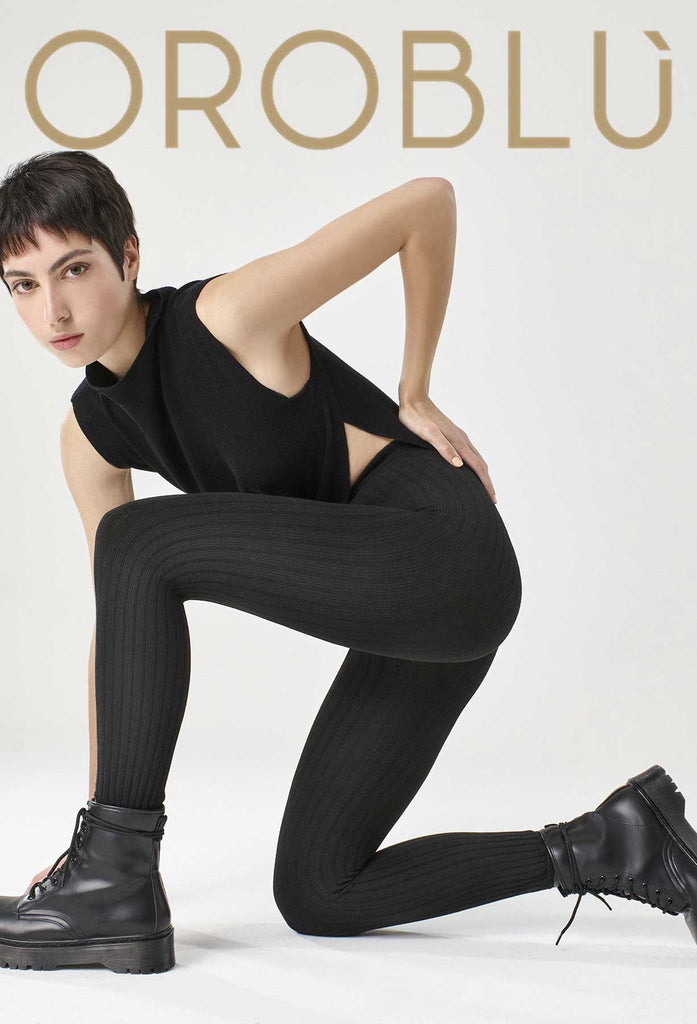 Lady, kneeling on one knee, wearing black leggings, boots and tank.