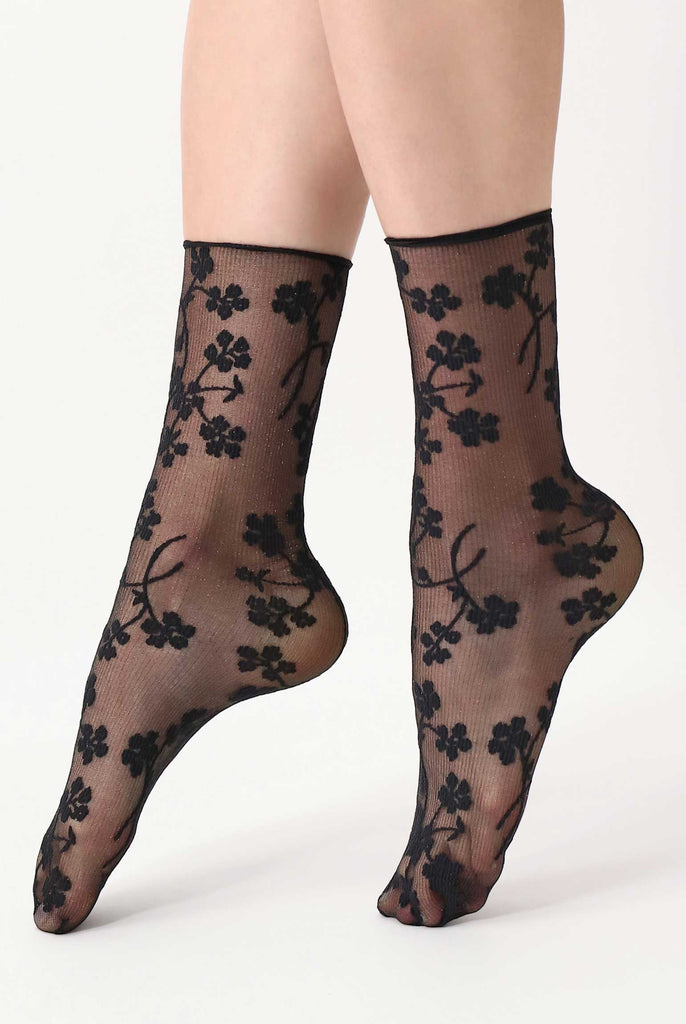 Ladies feet on tiptoes, wearing black floral pattern black, sheer, ankle socks.