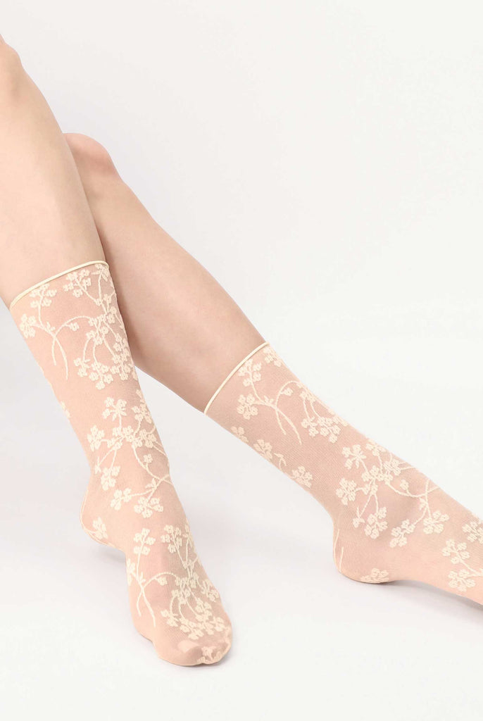 Ladies feet outstretched and wearing cream flower pattern, sheer, ankle socks.
