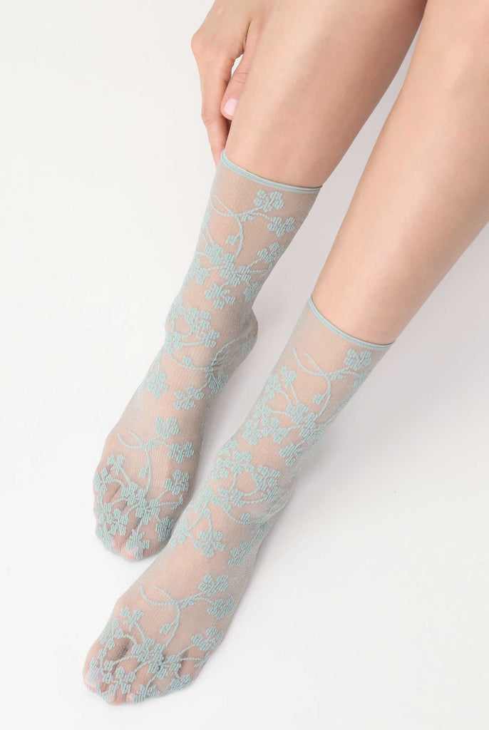 Ladies feet outstretched and wearing sheer flower pattern idro green ankle socks.