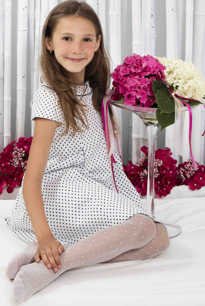 Young girl sitting side on wearing a dress and white spotty tights.