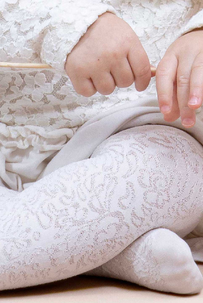 Close up of baby's legs in white floral tights.