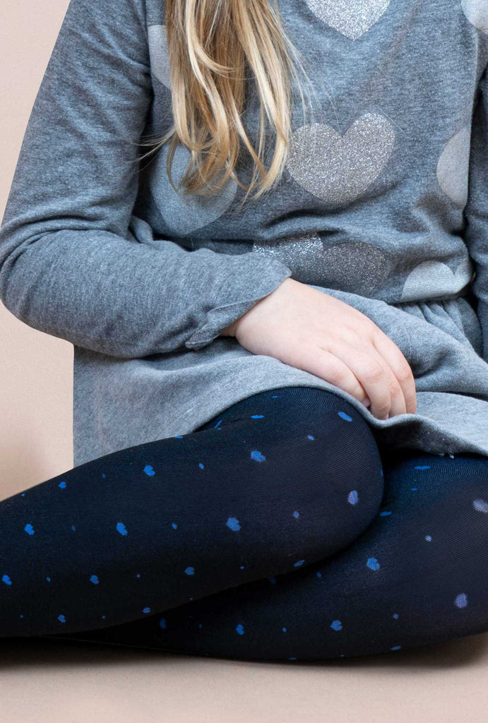 Close up of girls knees and legs, wearing blue heart pattern tights and grey top.