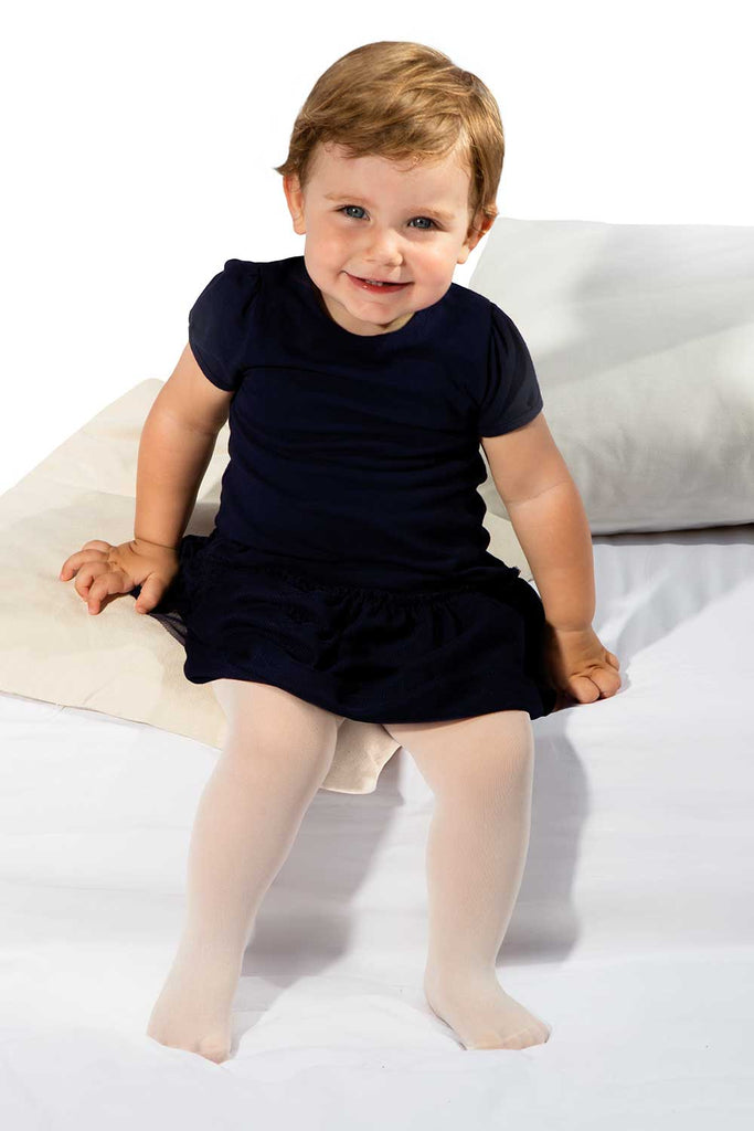 Baby girl sitting on cushions in white tights and black dress.