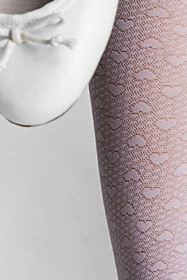 Close up of girl's leg wearing white sheer heart pattern tights against a white ballerina shoe.