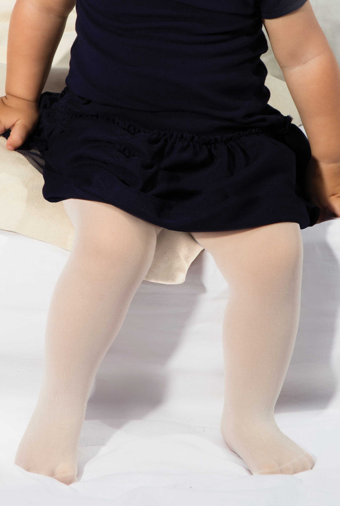 Close up of baby's legs in white plain knit tights and black dress.