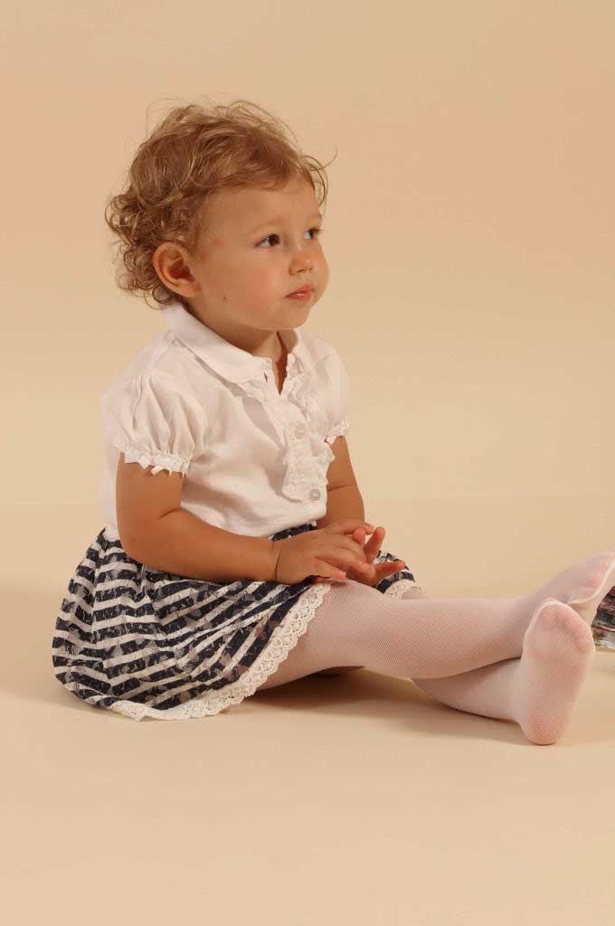 Baby girl, sitting with legs outstretched in white and black dress.