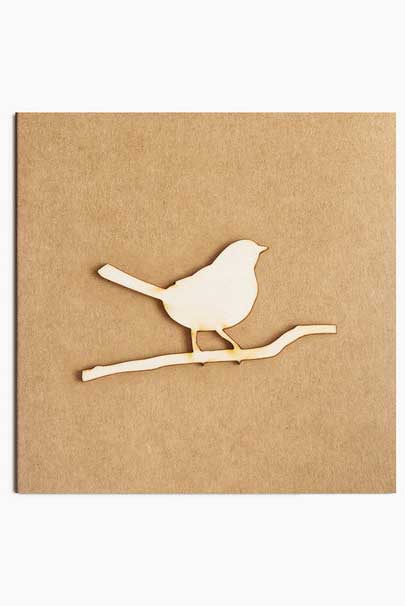 Wooden cut out bird perched on a branch on light brown card.