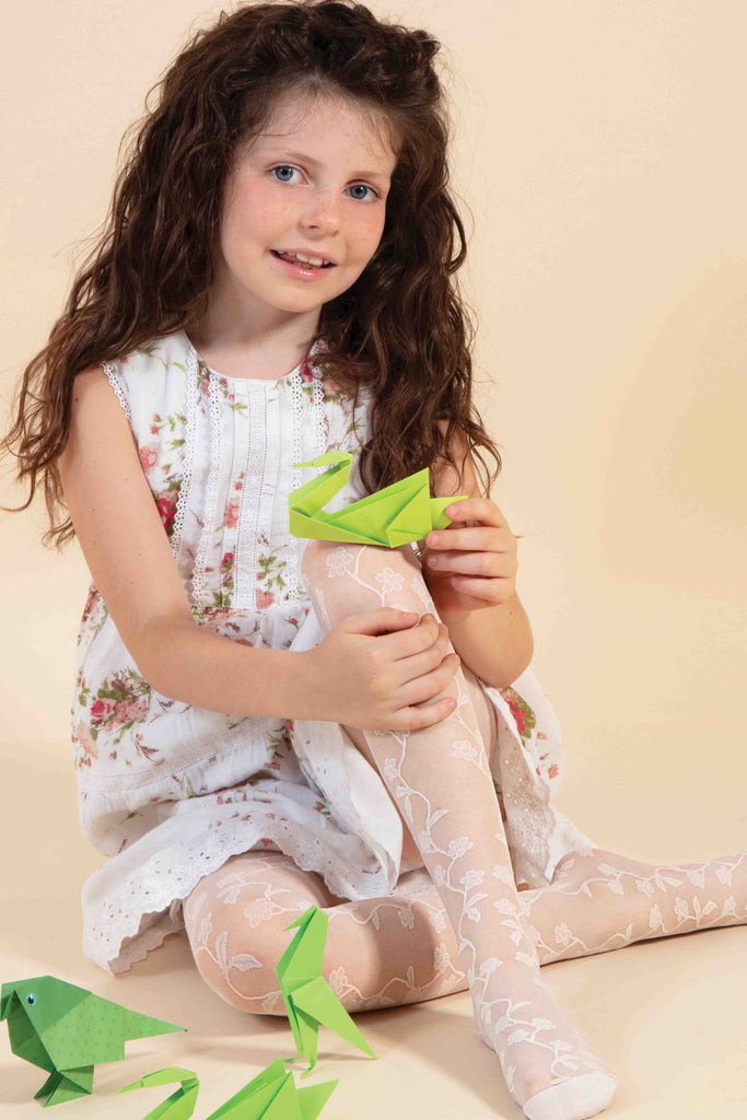 Young girl sitting, clutching her leg, in white floral tights.