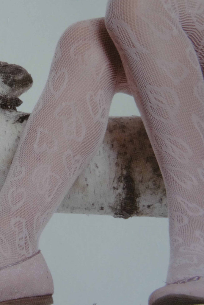 Close up of girls' legs in a sitting position wearing heart pattern lace mesh tights.