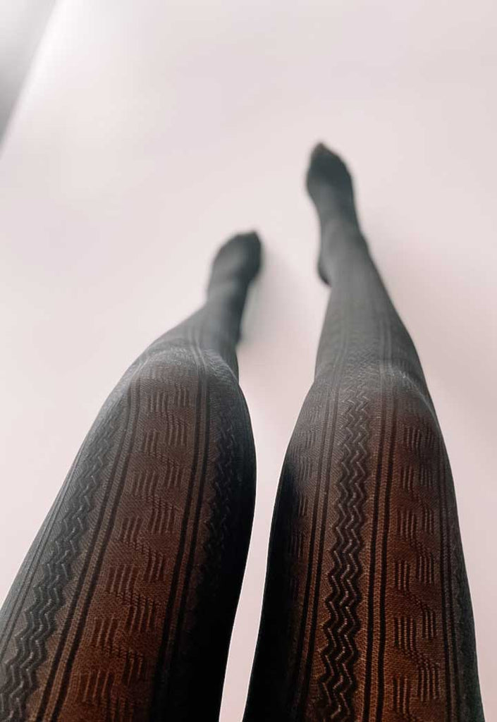 Lady's legs outstretched and wearing black cable knit tights.