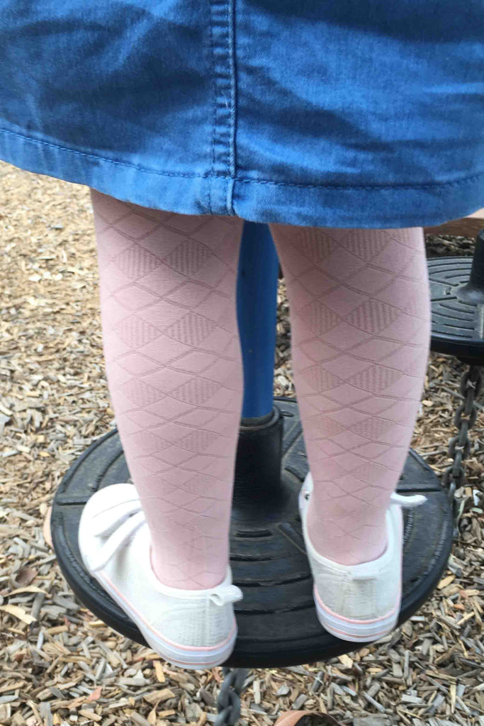 Back view of young girls legs in standing position wearing pink tights, white shoes and blue dress.