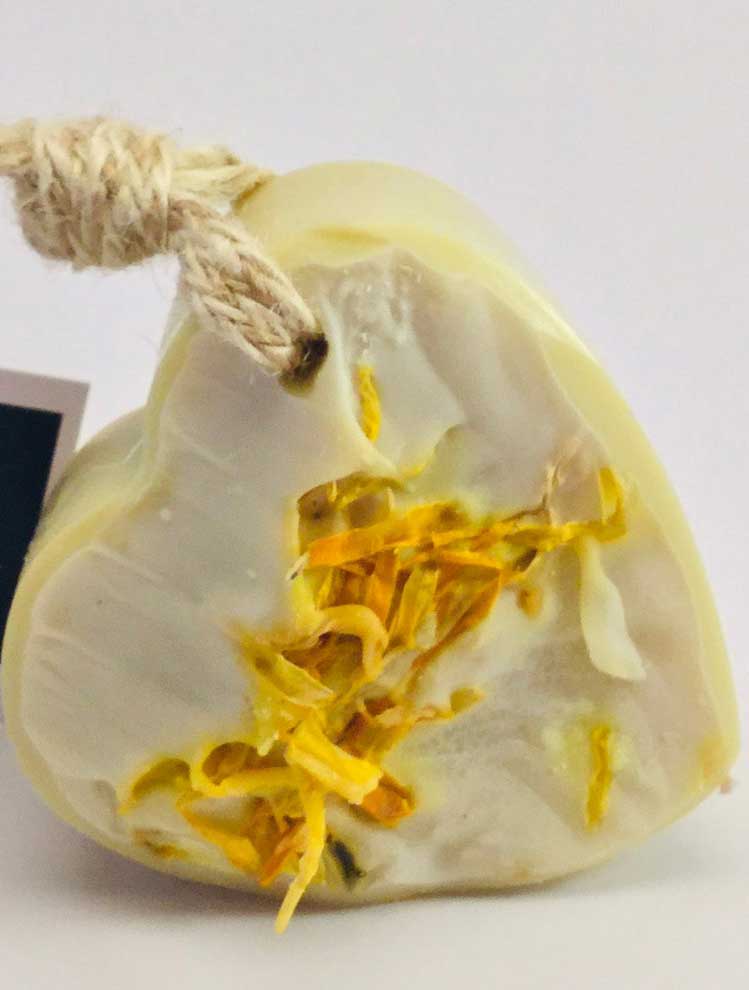 Close up of heart shape soap on a rope with yellow calendula petals.