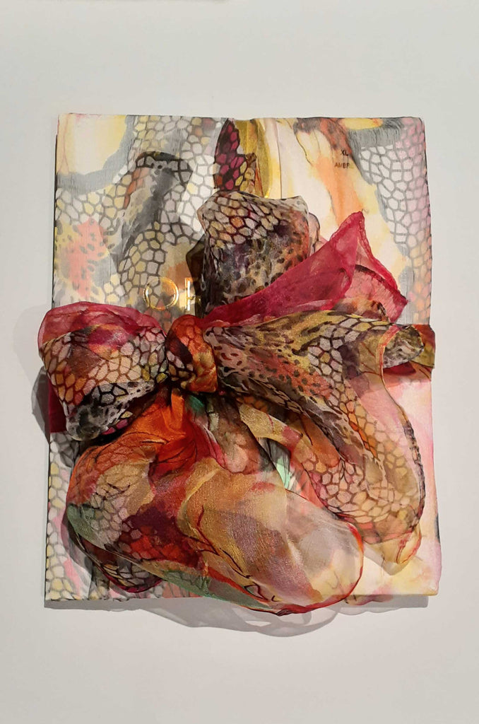 Orange toned sheer abstract pattern scarf used to as gift wrap around a gift.