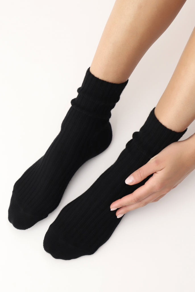 Lady's hand touching side of left foot wearing black socks.