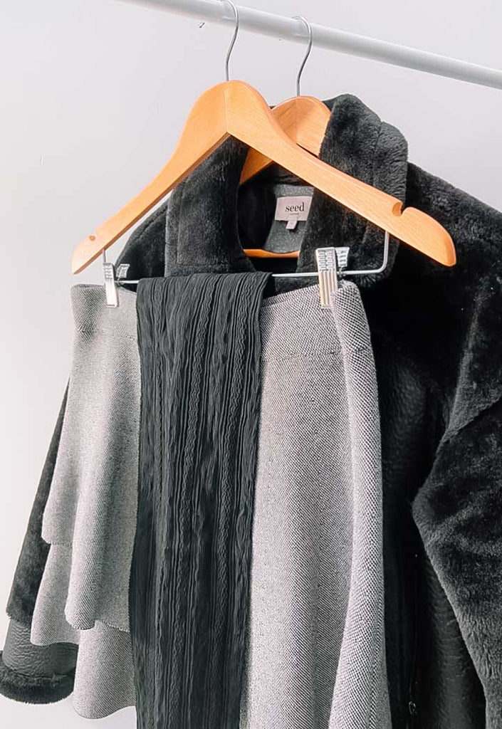Lady's black coat, grey skirt and cable knit tights hanging on clothes hangers.