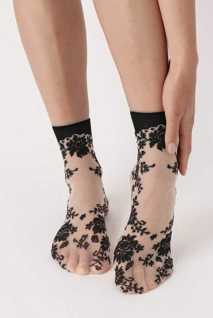 Lady's feet, caressed by her hand wearing sheer nude and black floral socks.