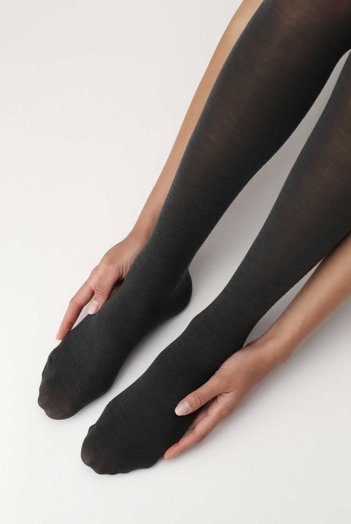 Lady holding the side of her feet in dark grey tights.