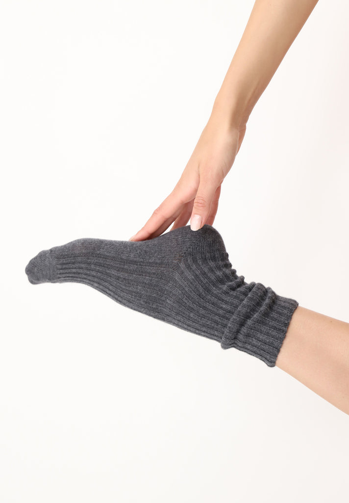 Lady's foot, in grey melange rib socks, kicked back in the air with her hand touching the sole.
