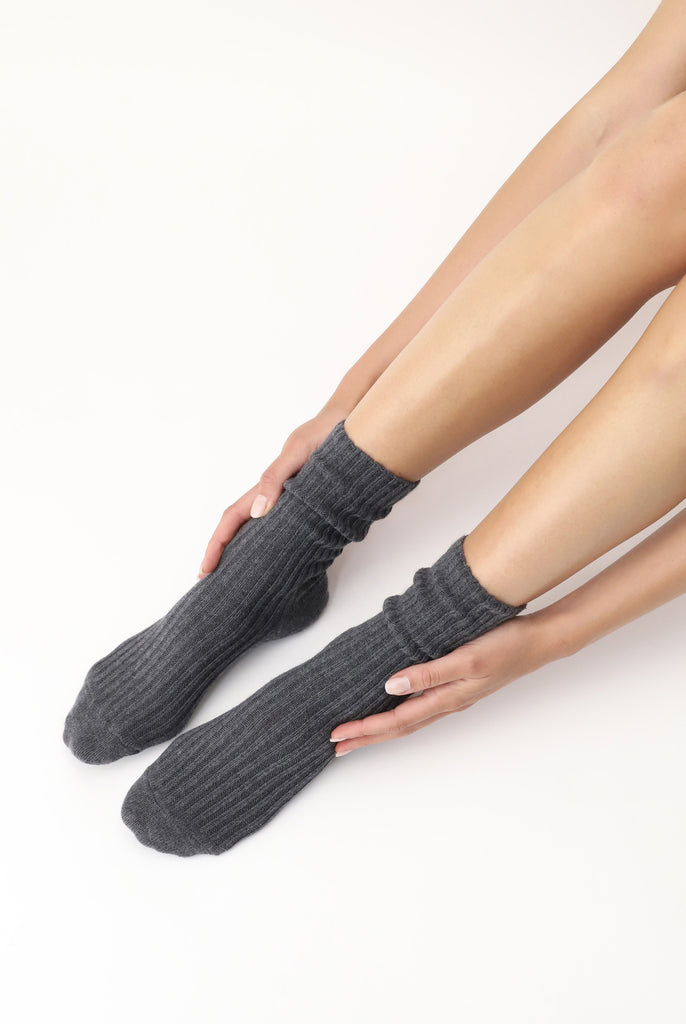 Lady's hands holding sides of feet, wearing grey melange socks.