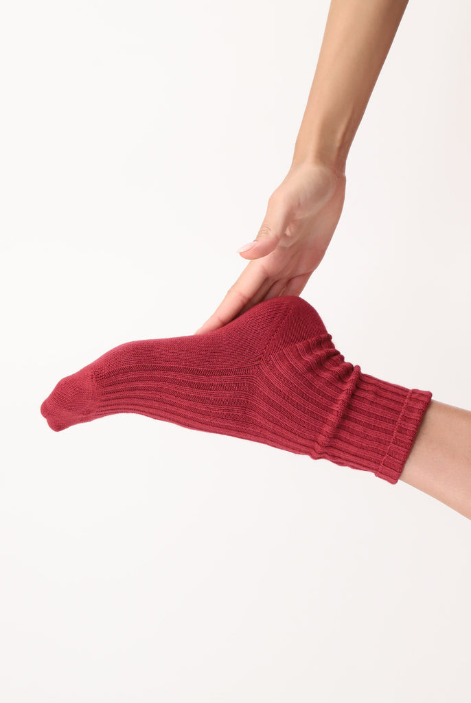 Lady's foot, in red rib socks, kicked back in the air with her hand touching  the sole.