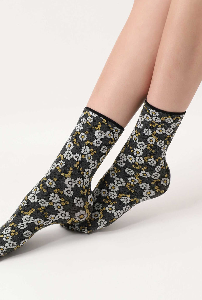 Women's crossed feet, outstretched and wearing white and green flowery print socks.