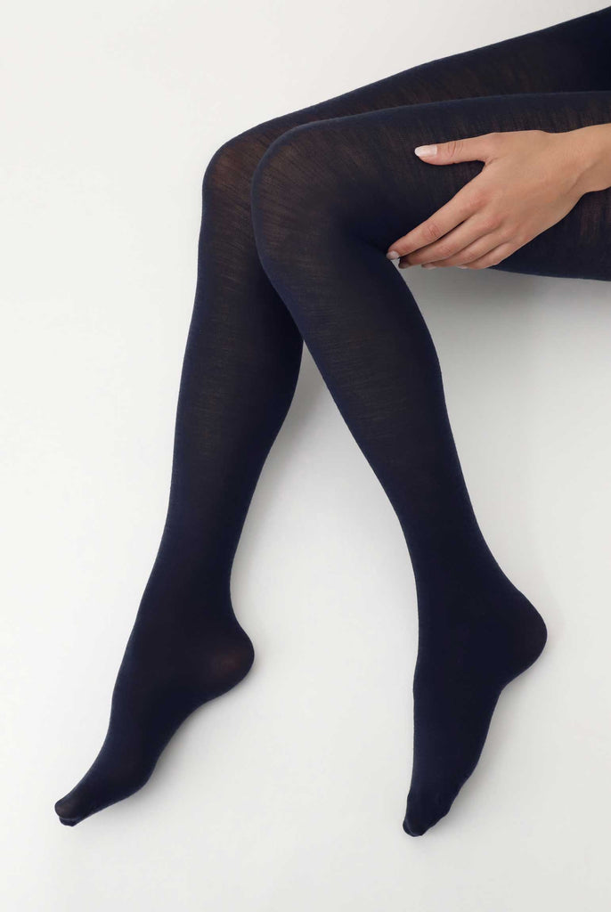 Side view of lady's legs, bent at the knees with one hand resting on an upper thigh, in navy tights.
